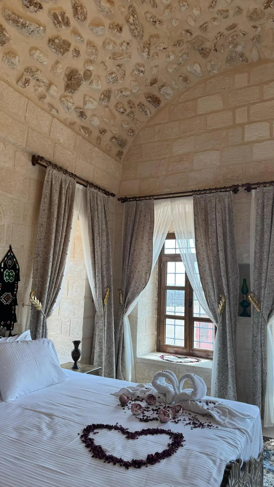 Una camera con letto, finestra con tende e soffitto in pietra
